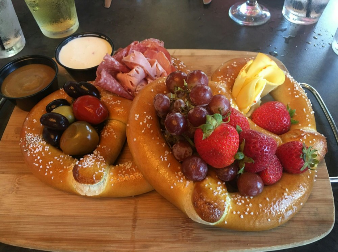 Soft pretzels on a cutting board with fruit and meats