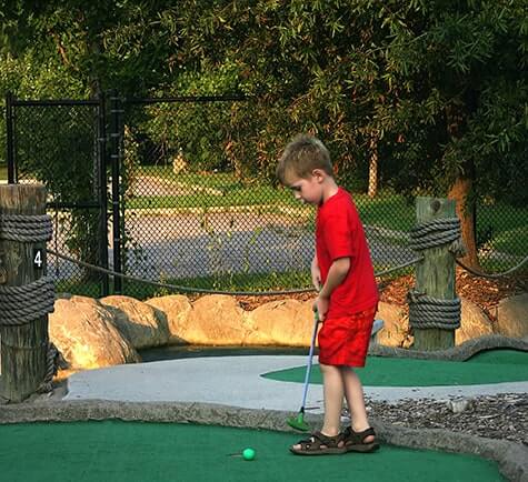 a blonde boy wearing a red outfit playing putt putt golf