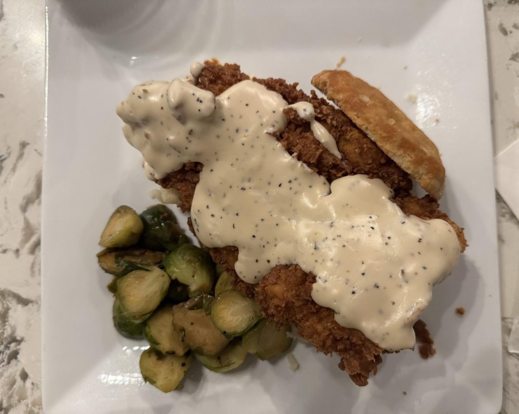 plated entree of a pork chop covered in gravy and served with brussel sprouts
