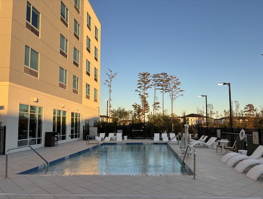 Image of a hotel building during sunset with a pool and lounge chairs