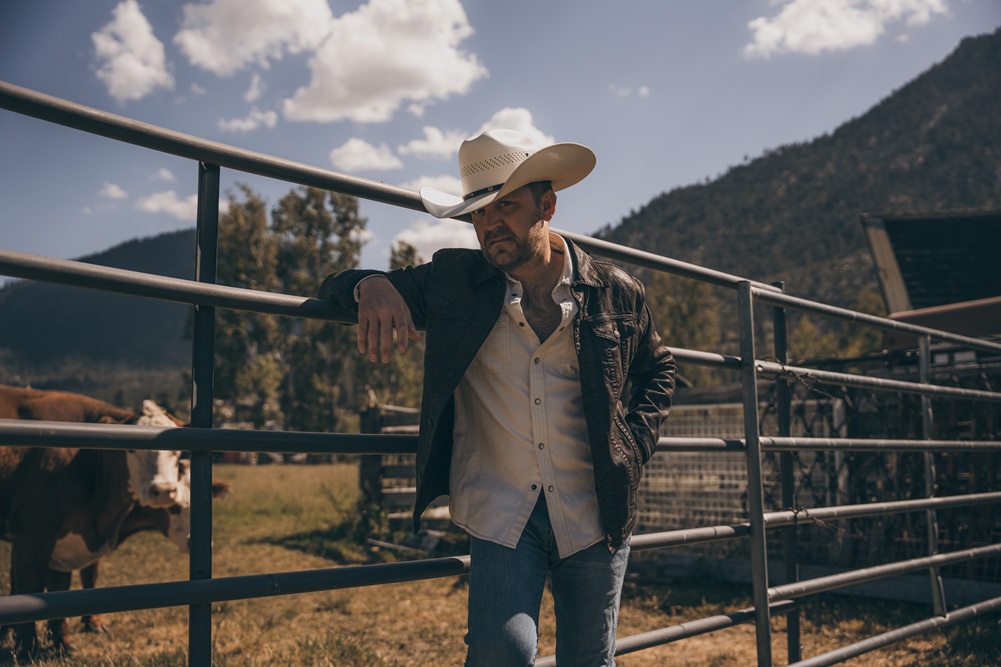Man in a cowboy hat standing in front of cows.