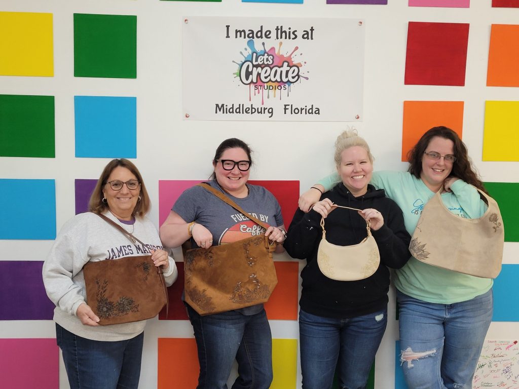 Ladies holding up purse creations at Let's Create Studios